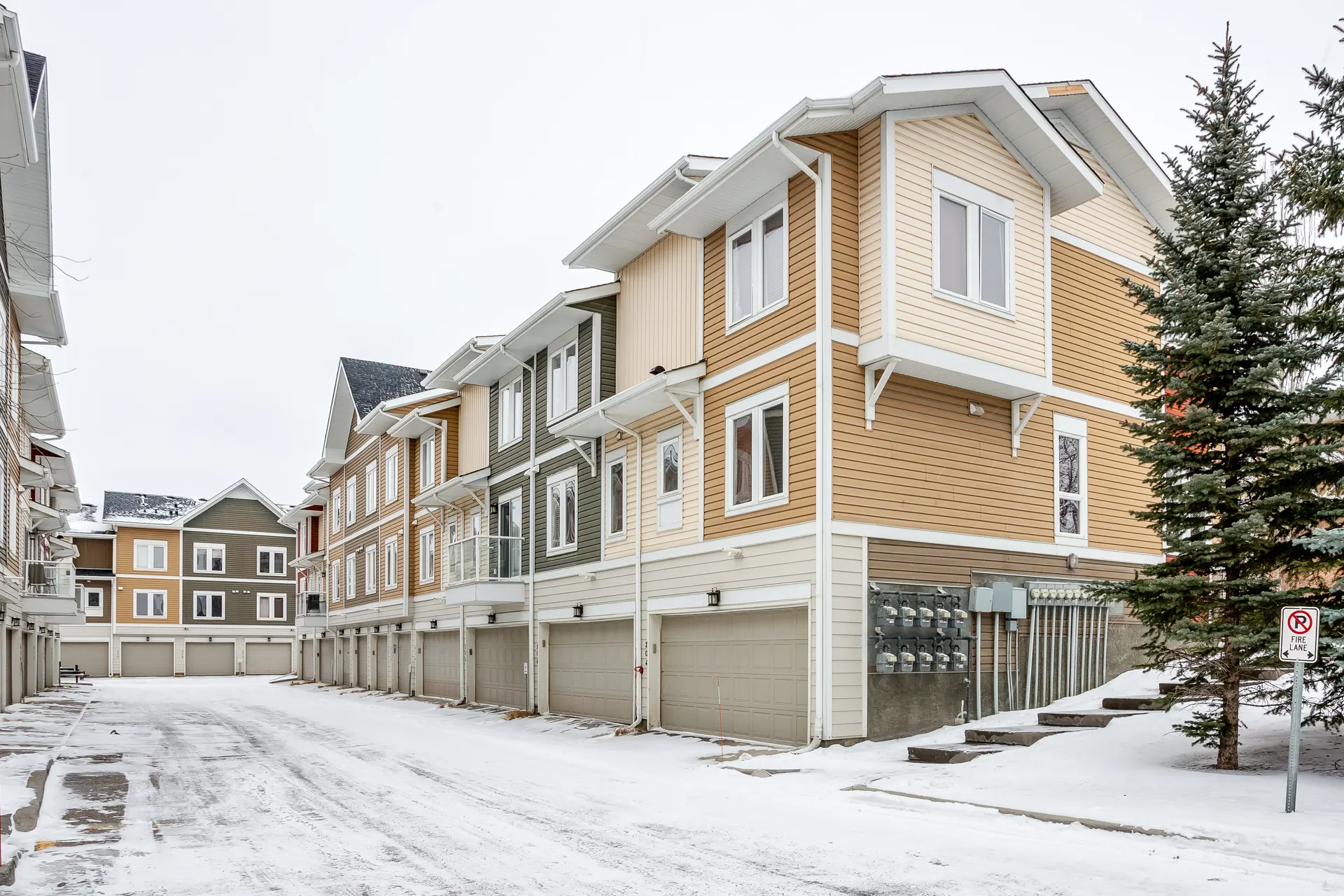 Snow-covered rear lane between townhome blocks in Auburn Bay