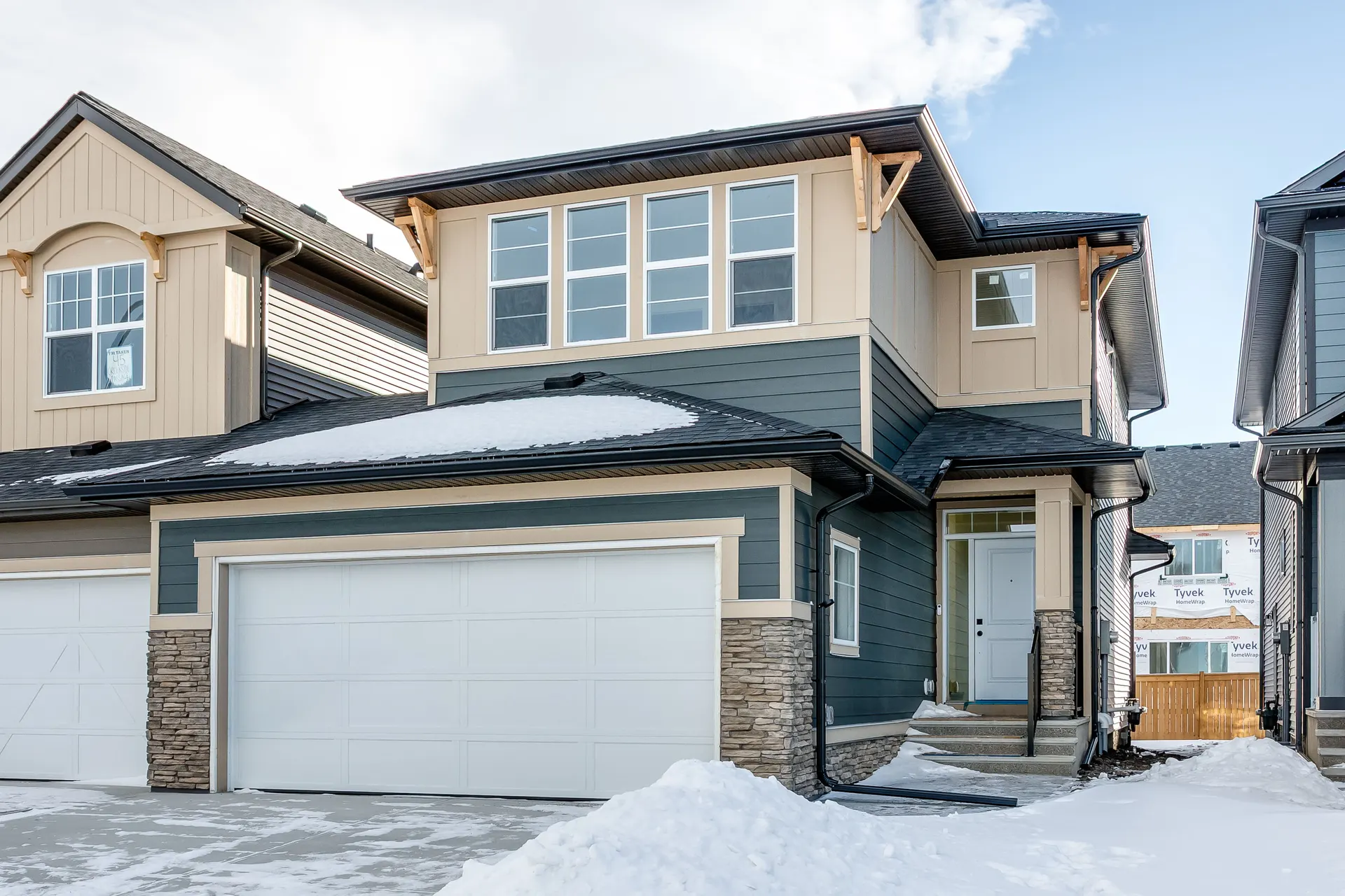 Newly built home with stone accents and attached garage in Pine Creek, Calgary SW